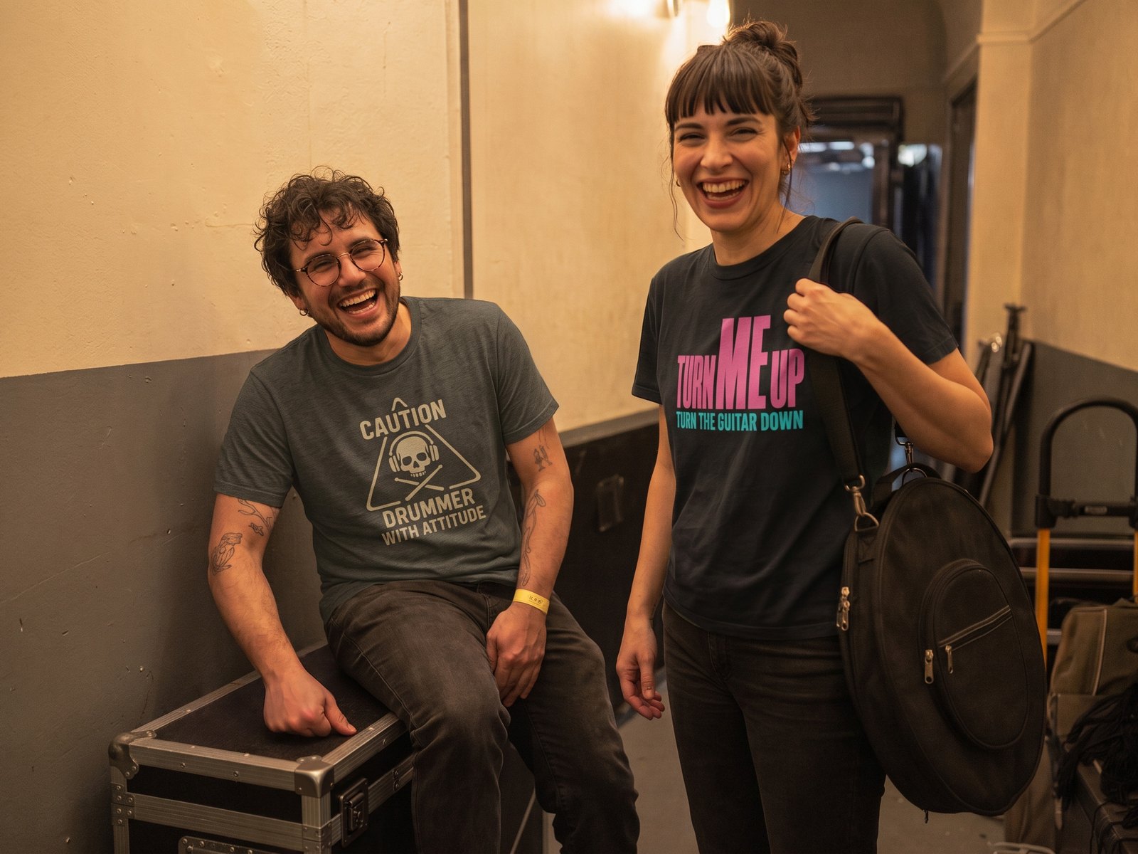 Two musicians laughing backstage, one in a Caution Drummer With Attitude t-shirt