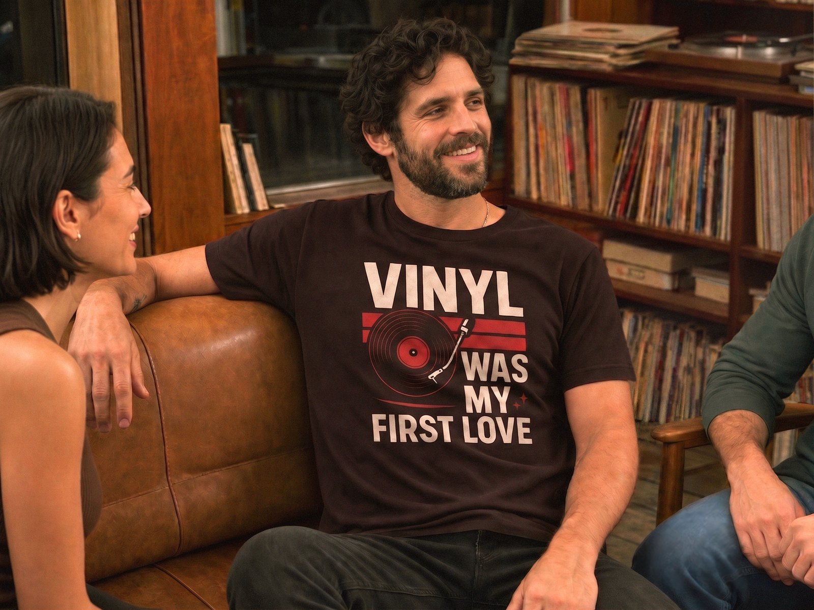 A man on a couch in a room lined with records, wearing a Vinyl Was My First Love t-shirt